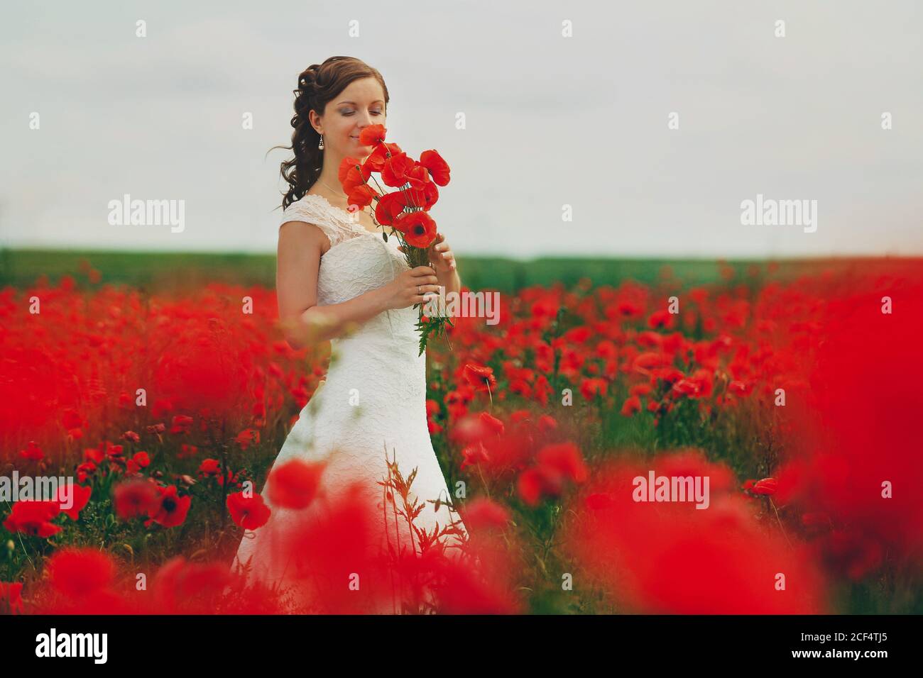 Braut in einem weißen Kleid mit Bouquet von roten Mohnblumen, warme Sonnenuntergangszeit auf dem Hintergrund der großen roten Mohnfeld. Speicherplatz kopieren. Das Konzept der Ruhe Stockfoto