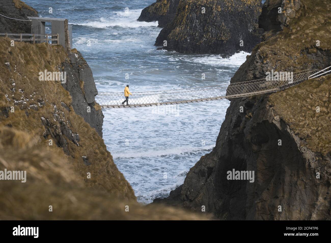 Von oben Seitenansicht des Reisenden, der über Carric A fährt Rede Hängebrücke zwischen felsigen Klippen und Meereswellen Absturz auf Felsen im Hintergrund Stockfoto