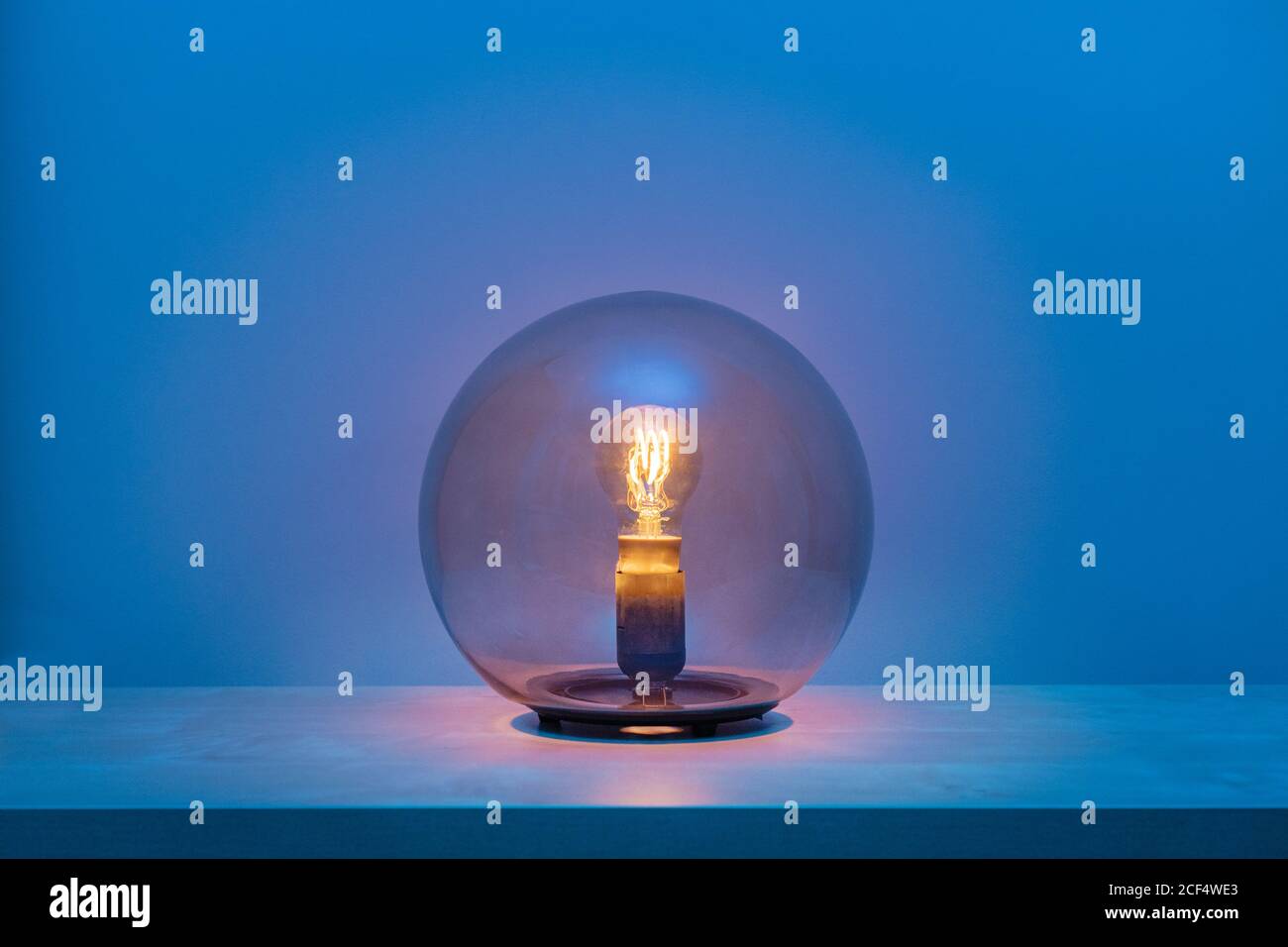Moderne eingeschwendete Leuchte mit Leuchtmittel innen dünn transparent Glaskugel in der Mitte des Regals im blauen Raum bei Abenddämmerung Stockfoto