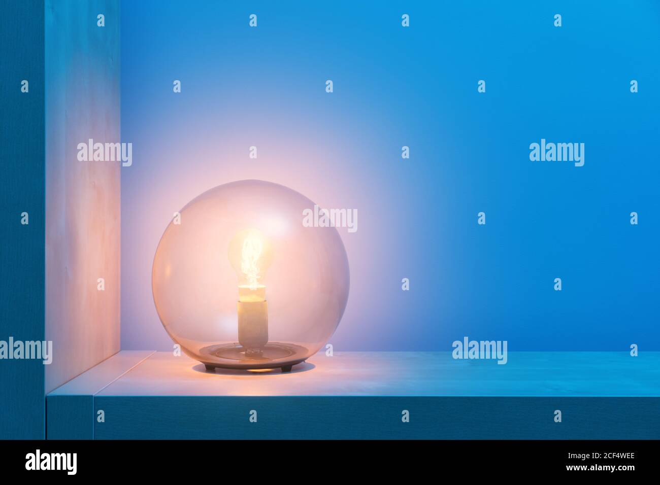 Stilvolle runde Lampe mit glühendem gelbem Licht im Inneren aus Glas Ball lokalisieren auf Regal in dunklen Raum mit blauen Wänden Stockfoto