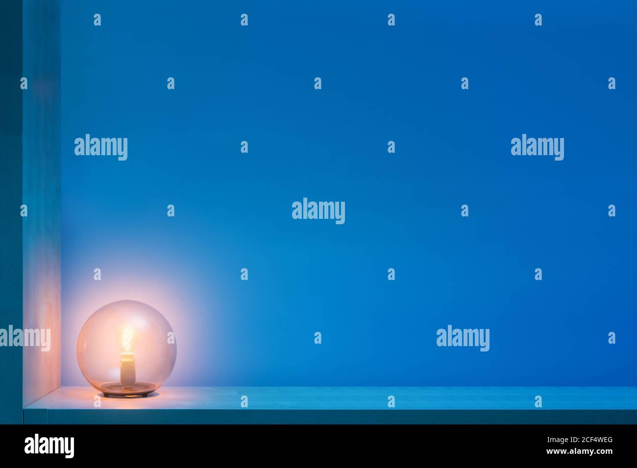 Stilvolle runde Lampe mit glühendem gelbem Licht im Inneren aus Glas Ball lokalisieren auf Regal in dunklen Raum mit blauen Wänden Stockfoto