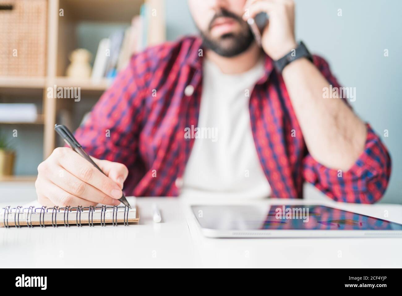 Ein anonymer Mann schreibt in einem Notizbuch. Der Mann arbeitet von zu Hause aus. Der Unternehmer spricht auf dem Handy Stockfoto