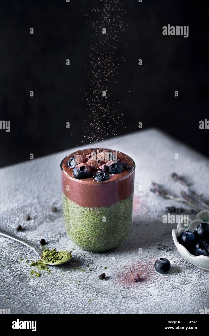 Ein Glas appetitlich gesunder Matcha-Tee und Chiasamen Smoothie Mit Schokolade und Heidelbeeren bestreut mit Kakaopulver auf Staub Mit Zuckerpulvertisch Stockfoto