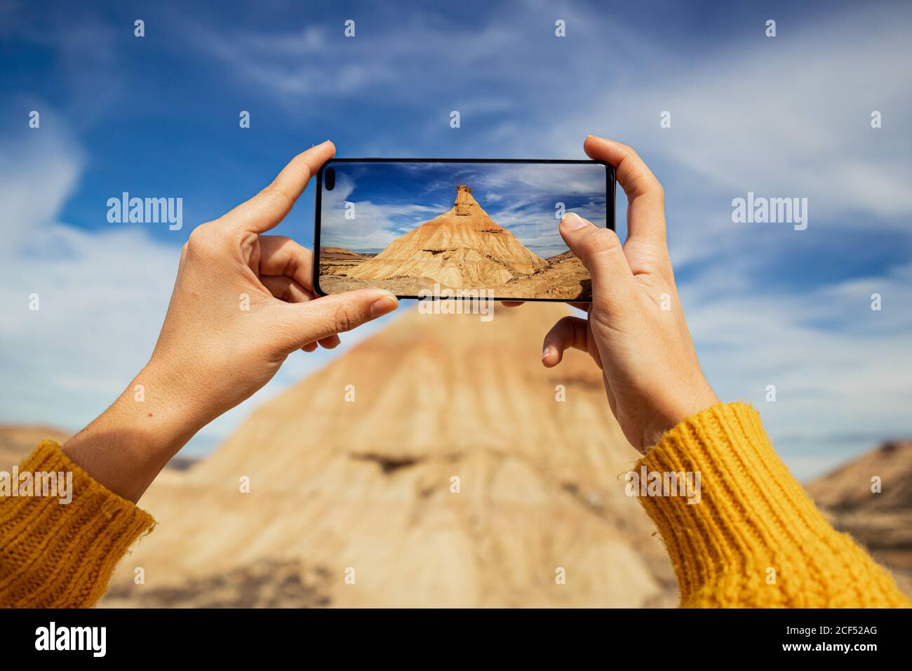 Crop weibliche Hände von anonymen Reisenden machen Bild von großen Braune Klippe mit buntem blauen Himmel und weißen Wolken auf Hintergrund bei Bardenas Reales in Spanien Stockfoto