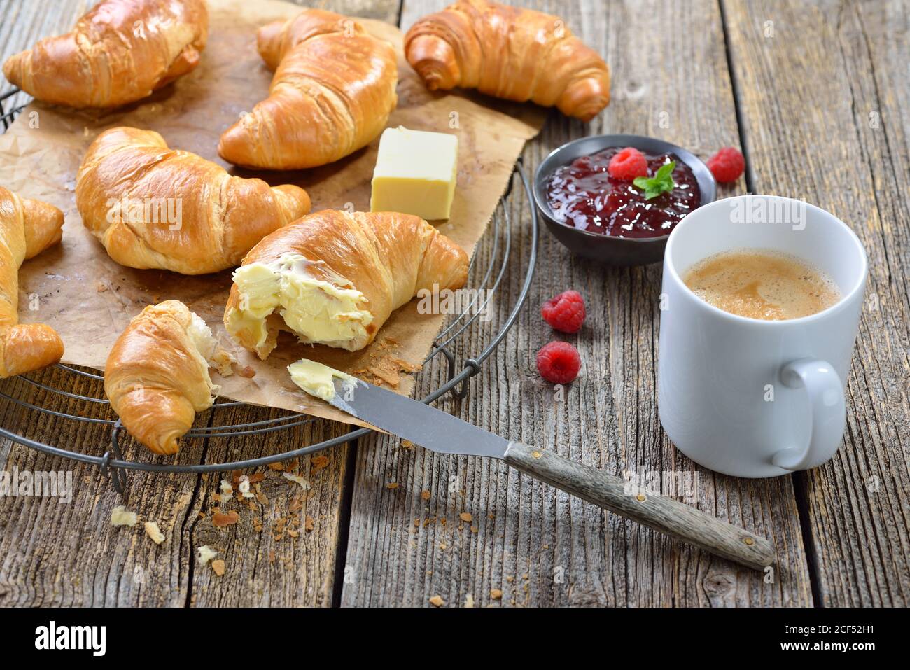 Frühstück mit frisch gebackenen Croissants auf einem Kühlregal, serviert mit Butter, Marmelade und einer Tasse Kaffee-Creme Stockfoto