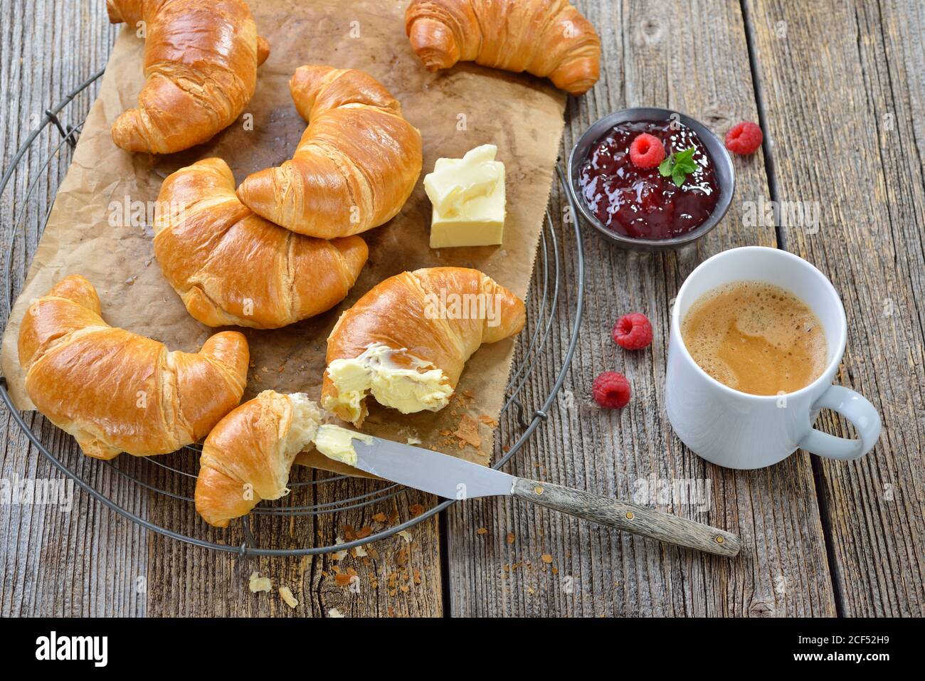 Frühstück mit frisch gebackenen Croissants auf einem Kühlregal, serviert mit Butter, Marmelade und einer Tasse Kaffee-Creme Stockfoto