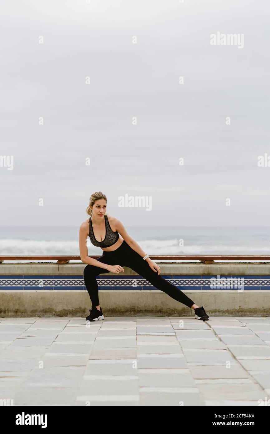 Motivierte, sportliche Frau in aktiver Kleidung, die die Beine im Stehen dehnt, während sie wegschaut Stockfoto