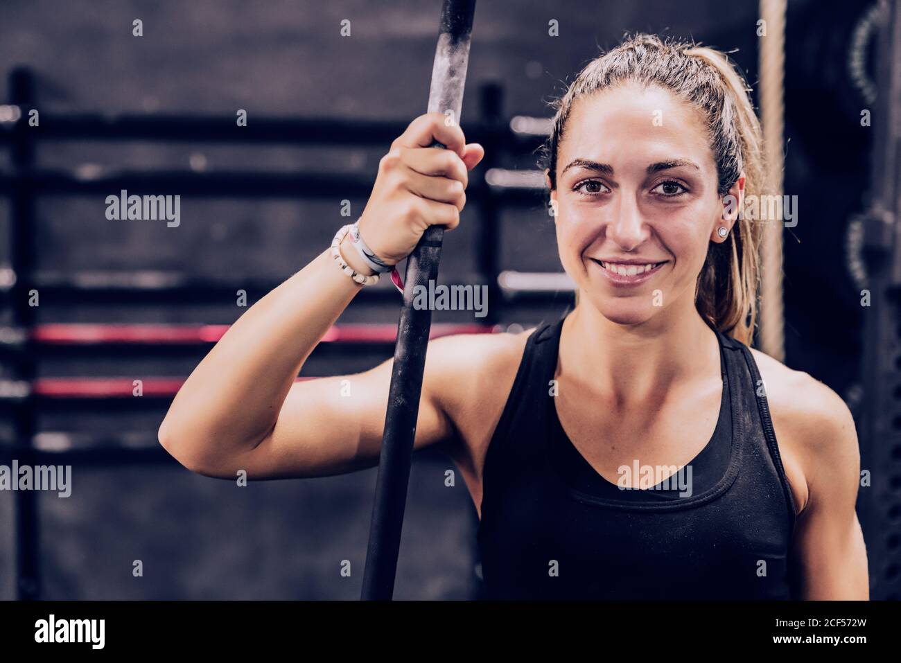 Friedliche schlanke weibliche mit Ruhe mit Stange Blick auf Kamera im Fitnesscenter auf unscharfem Hintergrund Stockfoto