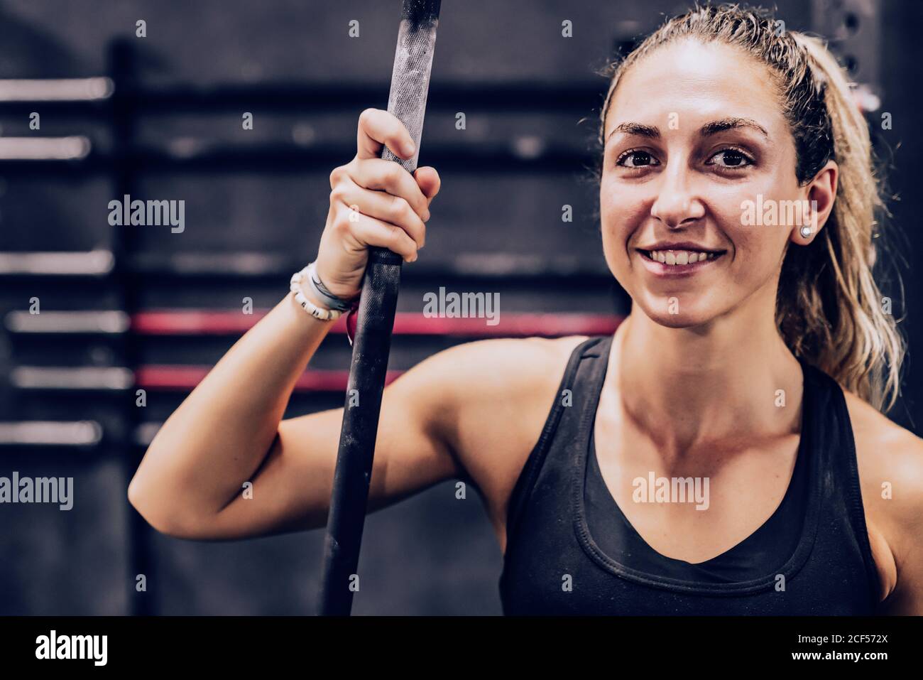 Friedliche schlanke weibliche mit Ruhe mit Stange Blick auf Kamera im Fitnesscenter auf unscharfem Hintergrund Stockfoto
