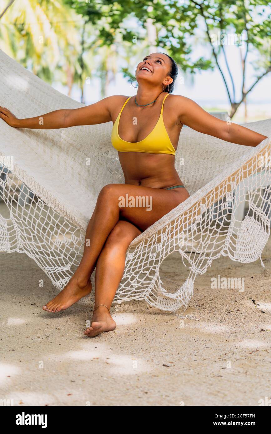 Entzückte Frau im Badeanzug, die in der Hängematte sitzt und auf die exotische Küste in Costa Rica blickt Stockfoto