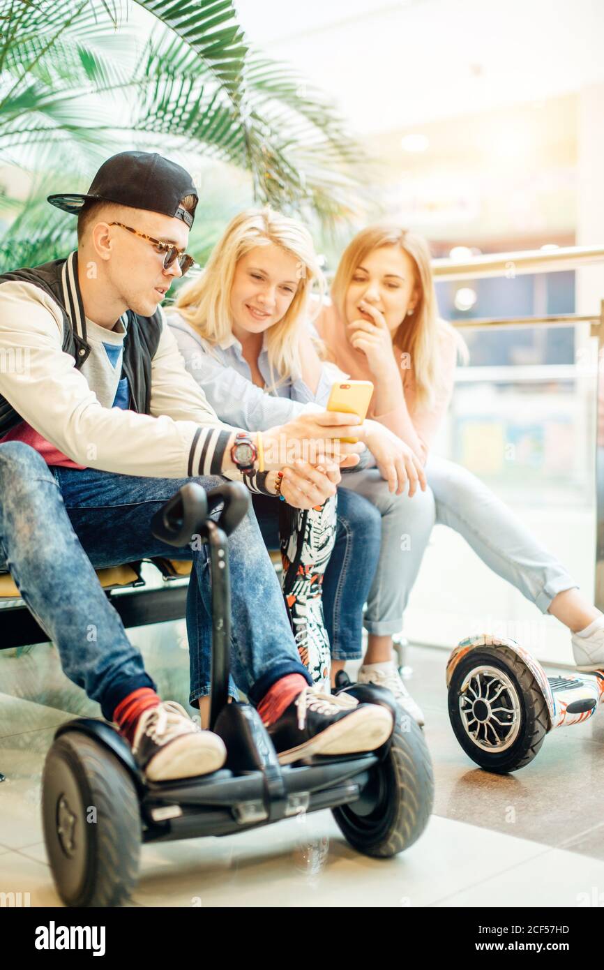 Gruppe der modernen Menschen mit elektrischen scooter Hoverboard an Bank sitzen und mit Hilfe von Phone Stockfoto