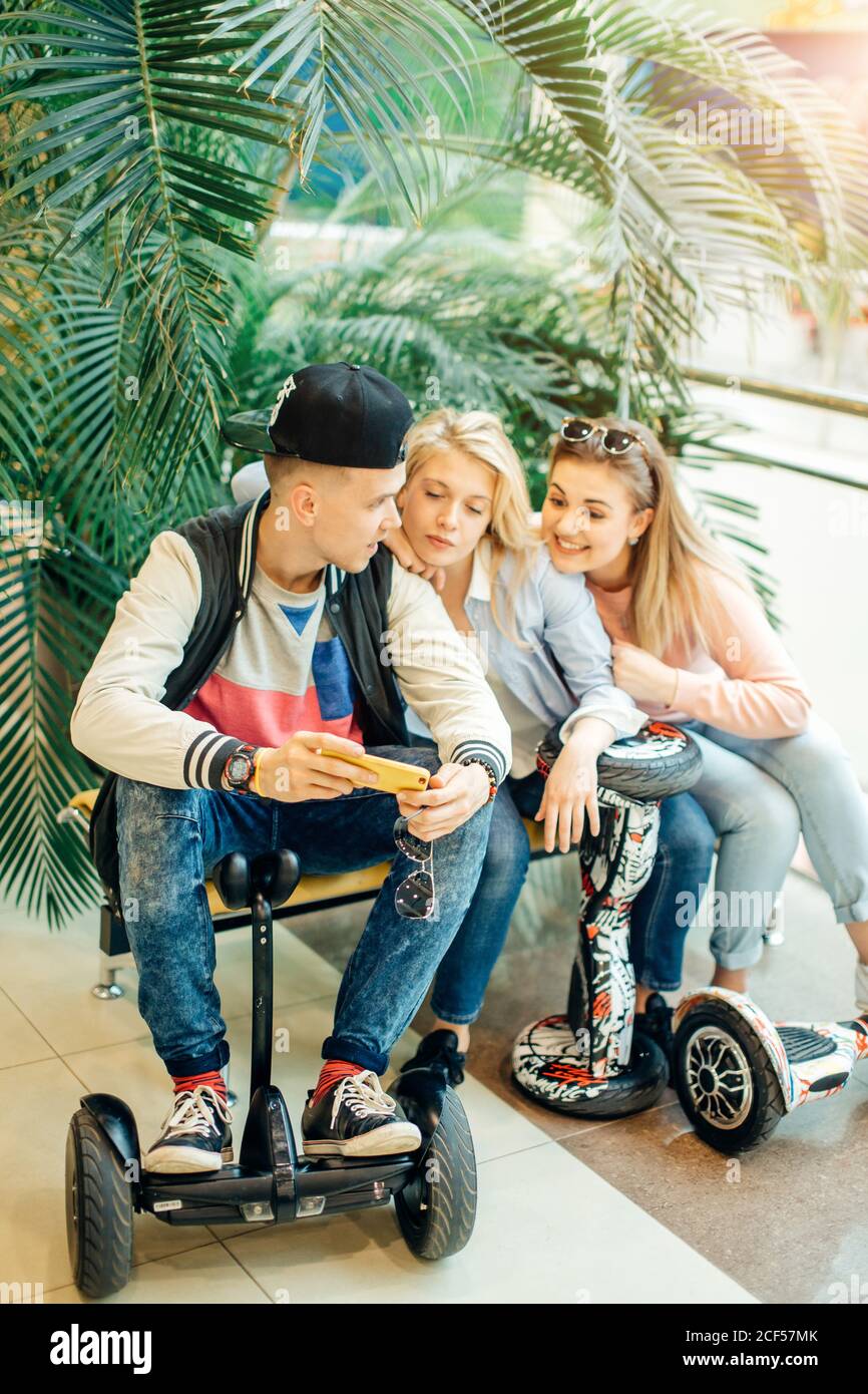 Gruppe der modernen Menschen mit elektrischen scooter Hoverboard an Bank sitzen und mit Hilfe von Phone Stockfoto