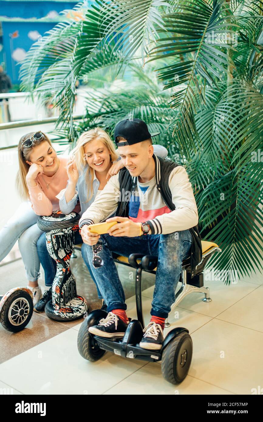 Gruppe der modernen Menschen mit elektrischen scooter Hoverboard an Bank sitzen und mit Hilfe von Phone Stockfoto