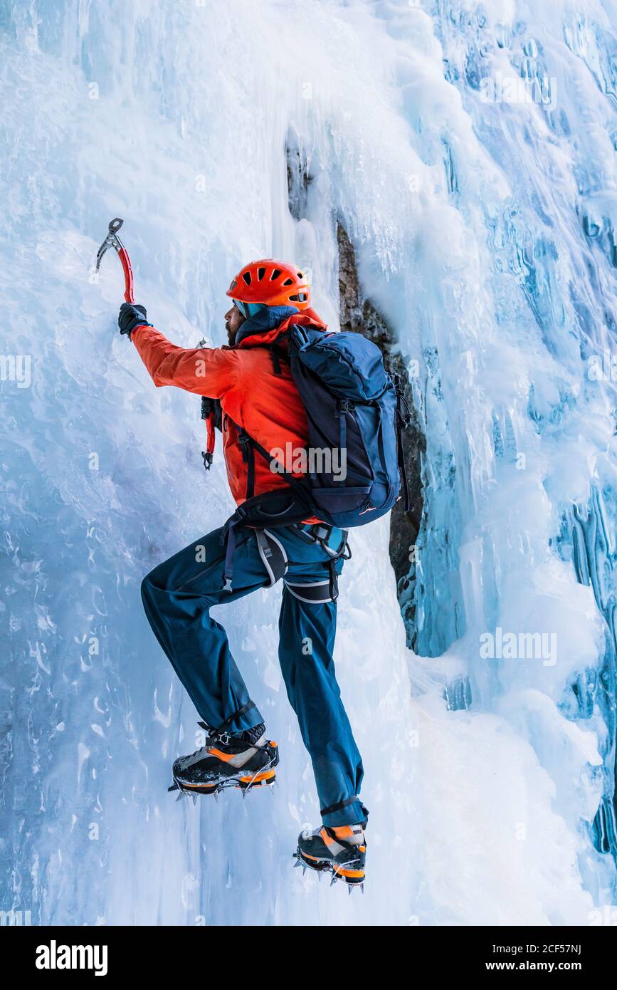 Rückansicht der Person in warmer Kleidung mit Rucksack Verwendung Werkzeuge, um gefrorenen Berggletscher zu klettern Stockfoto