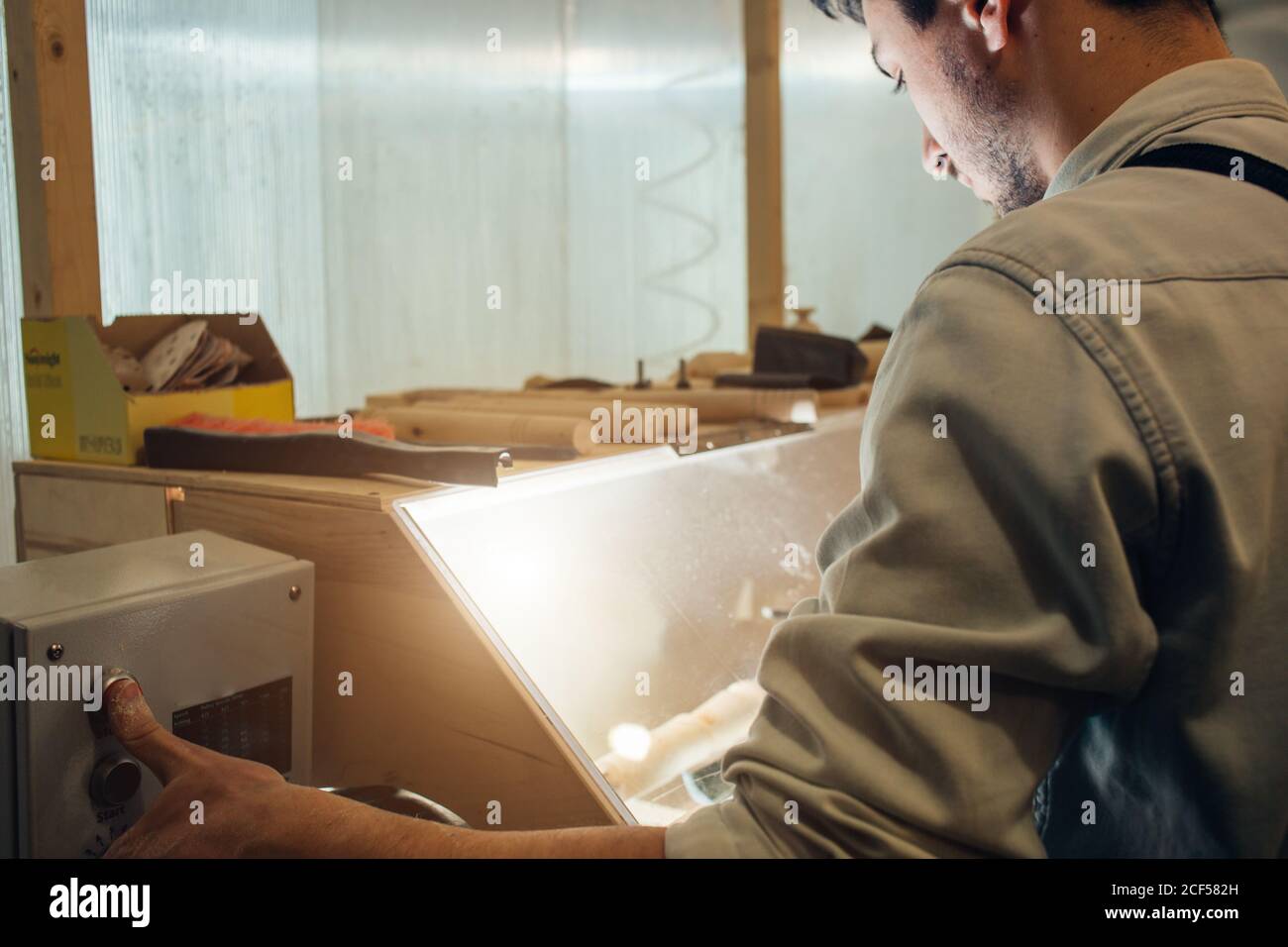 Mann in einer grauen Kappe Zimmermann Baumeister in Arbeitskleidung Verarbeitung eines Baumes mit einer Fräsmaschine in der Werkstatt, um eine Menge Ausrüstung, Holzbretter Stockfoto