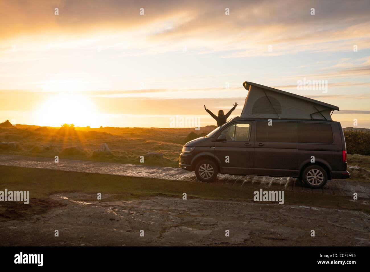Mann Silhouette mit öffnenden Händen, während auf Wohnwagen Anhänger auf einsamen Landstraße bei Sonnenuntergang in Wales stehen Stockfoto