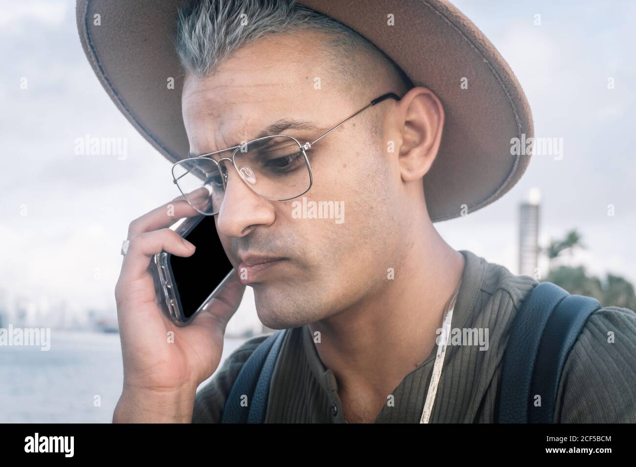 Junger Mann mit Hut und Gespräch am Handy mit besorgten Ausdruck. Hochformat Stockfoto