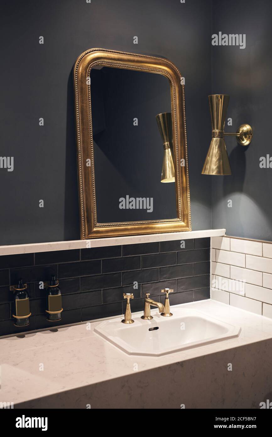 Spiegel mit goldenem Rahmen, der an der schwarzen Wand in der Nähe der Lampe  hängt Über Marmorabtheke mit Waschbecken im eleganten Badezimmer  Stockfotografie - Alamy