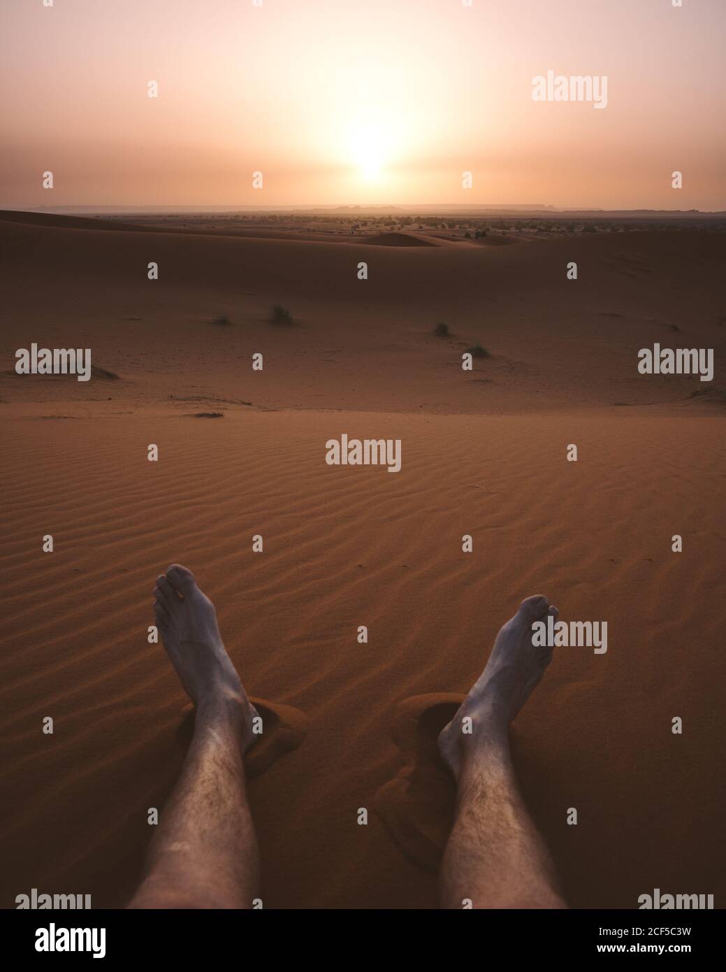 Crop männlichen barfuß Beine auf Sand der endlosen Wüste Düne in trüben Licht des Sonnenuntergangs, Marokko Stockfoto
