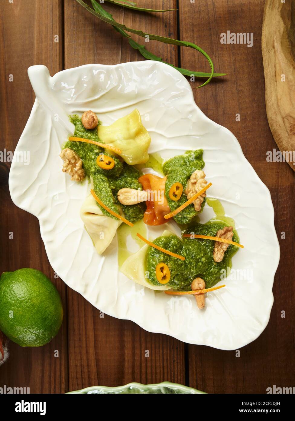 Blick von oben auf handwerkliche Ravioli Pasta mit Kräutersauce serviert Und Muttern auf Blatt geformten Platte auf Holztisch Stockfoto