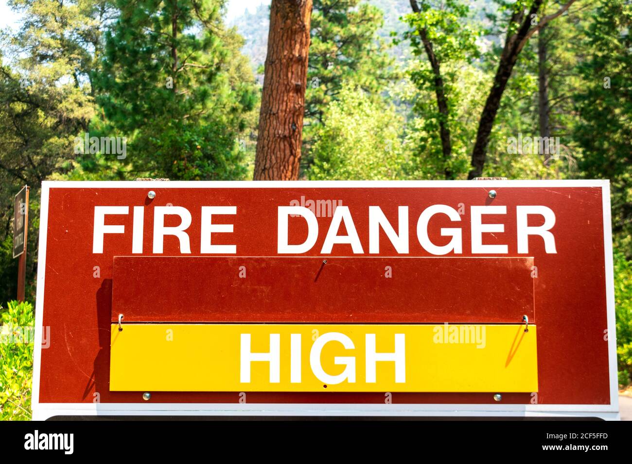 Ein Warnschild mit hoher Brandgefahr informiert die Öffentlichkeit darüber, dass es wahrscheinlich ist, dass es zu Waldbränden kommt. Grüner Wald Hintergrund. Stockfoto