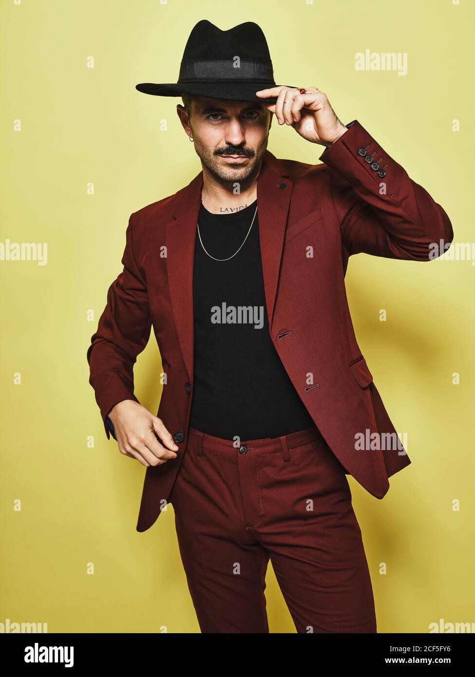 Schöner bärtiger gut gekleideter Rüde in modischem Weinanzug und hat schaut auf Kamera vor gelbem Hintergrund Stockfoto
