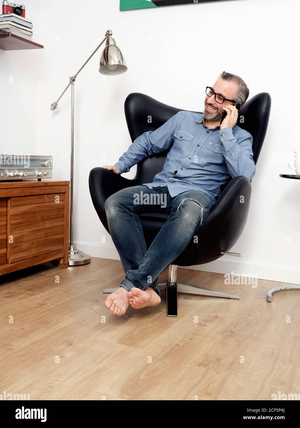 Mann im Gespräch auf dem Handy lächeln mit einem entspannten Kaffee im Sessel zu Hause Stockfoto