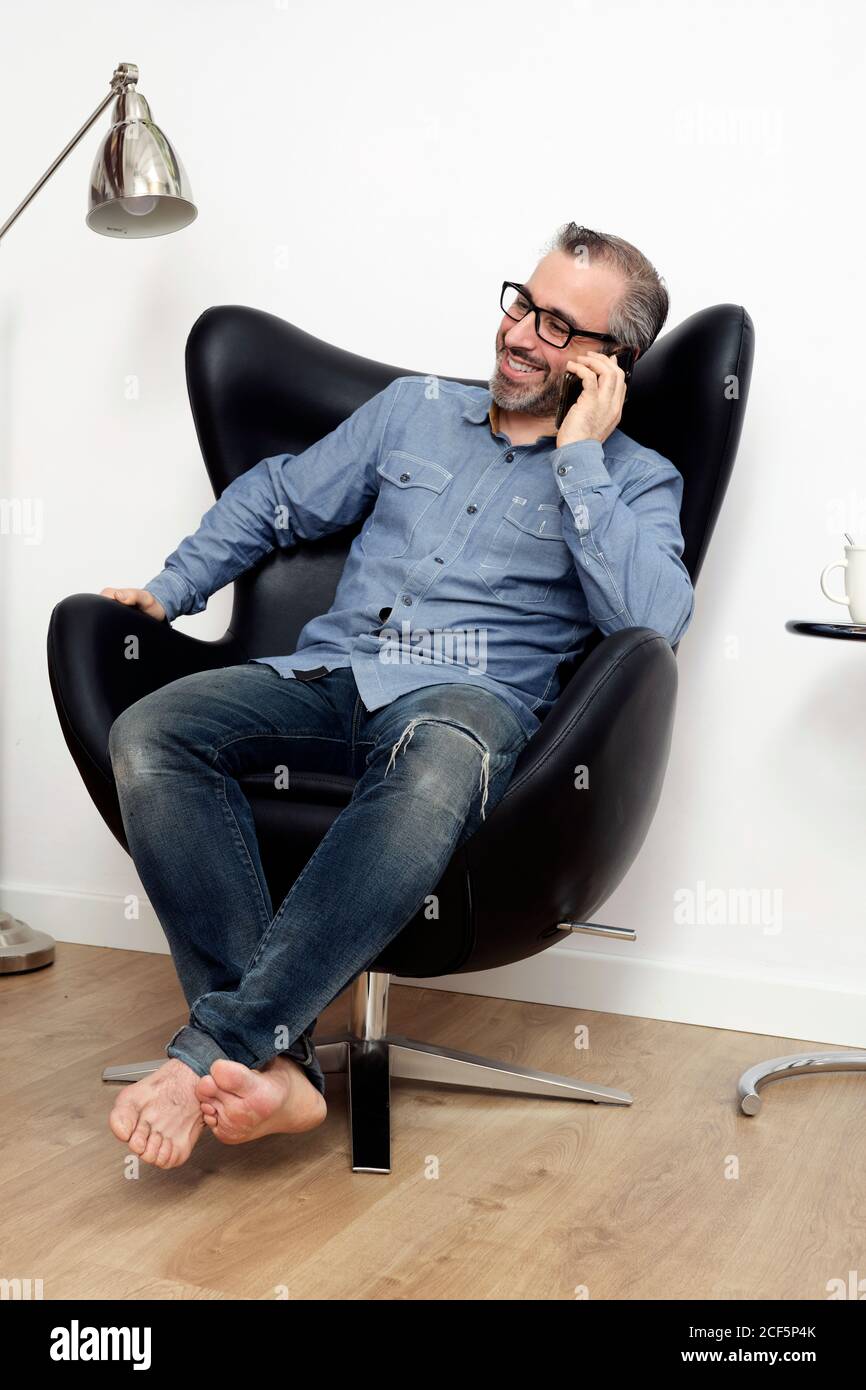 Mann, der lächelt am Telefon vom Sofa aus Zu Hause Stockfoto