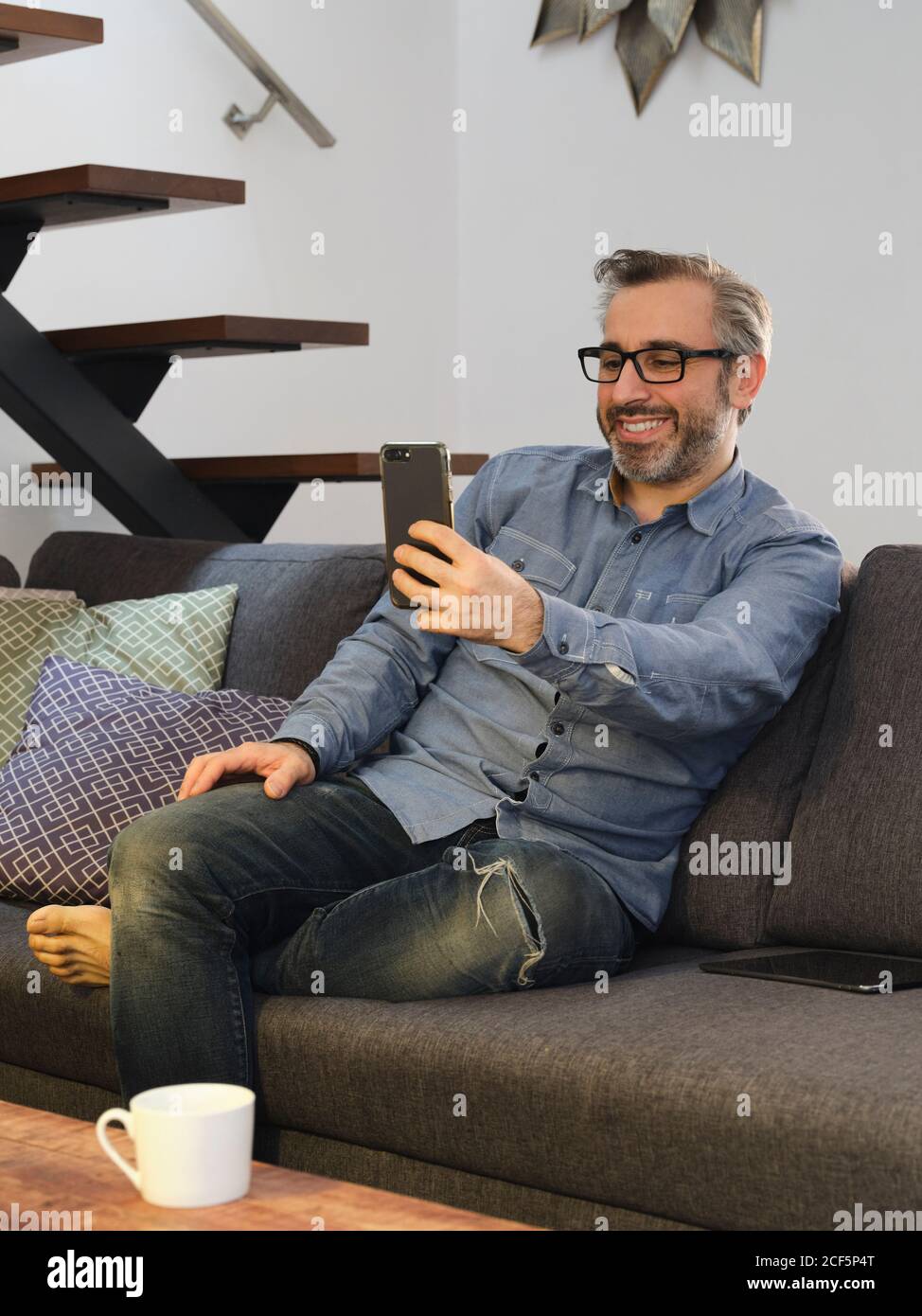 Mann, der lächelnd auf der Videokonferenz am Telefon von spricht Das Sofa zu Hause Stockfoto