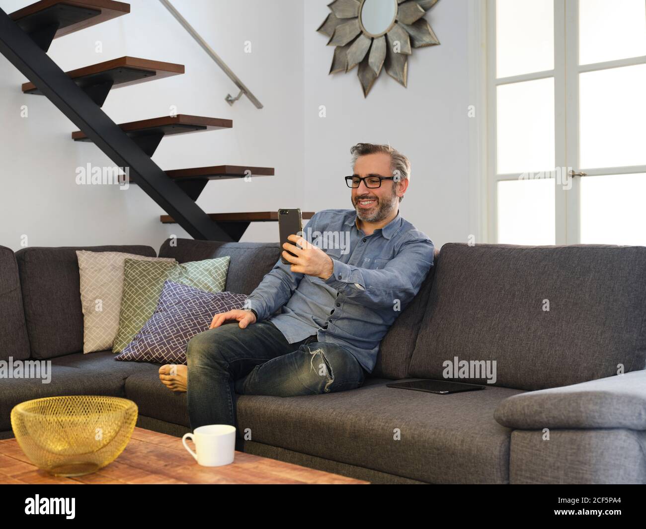 Mann, der lächelnd für eine Videokonferenz sprach, mit dem Telefon allein auf dem Sofa im Wohnzimmer zu Hause Stockfoto