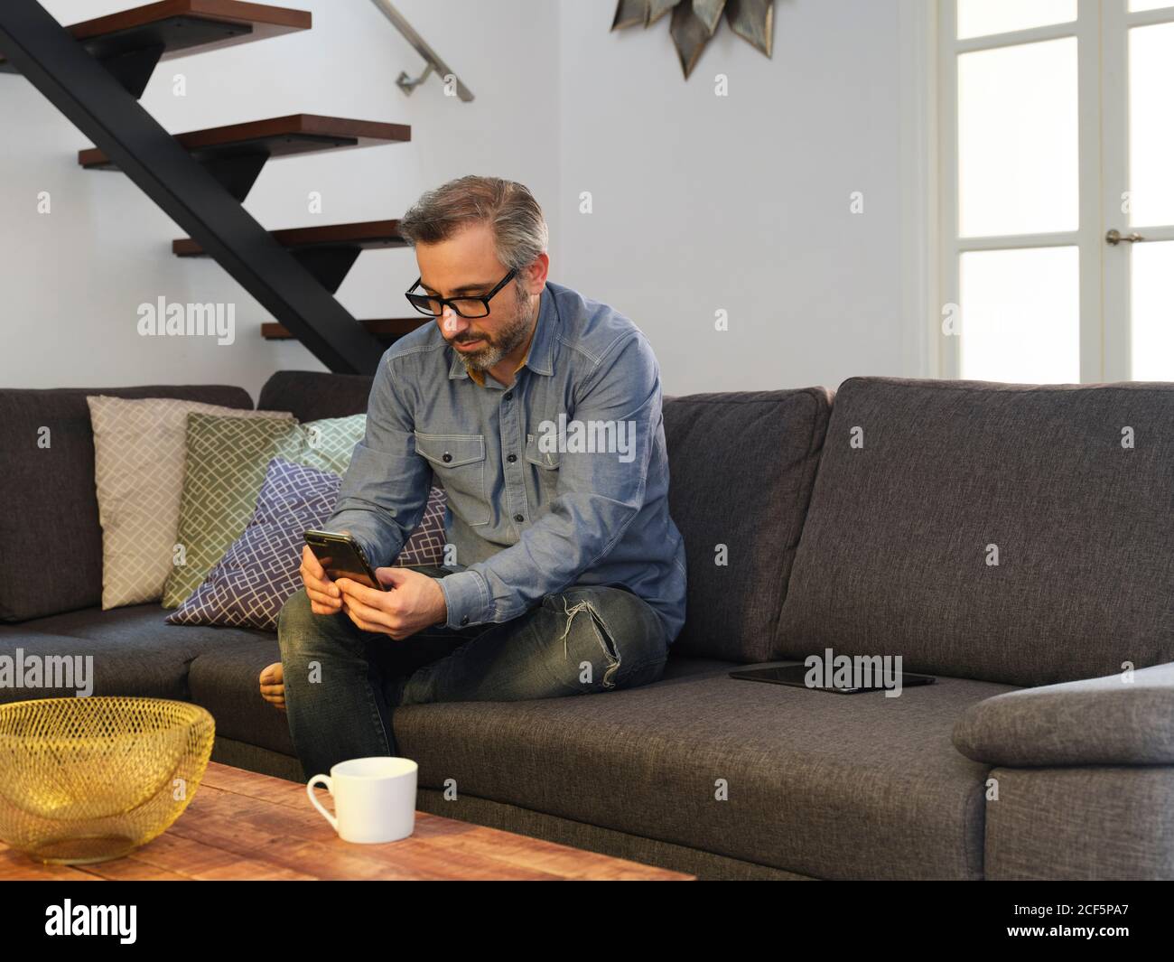 Mann, der alleine auf dem Sofa im Wohnzimmer zu Hause telefonieren kann Stockfoto