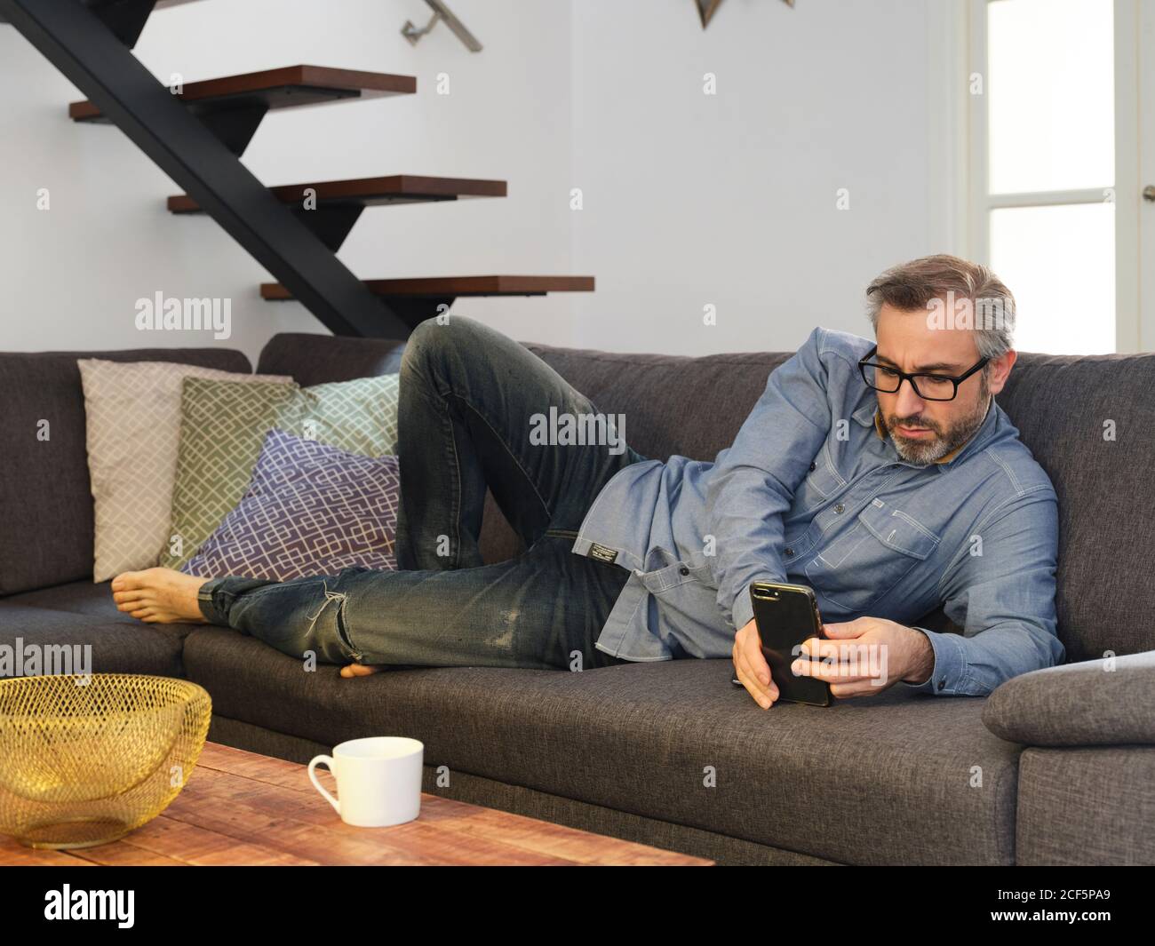 Mann, der alleine auf dem Sofa im Wohnzimmer zu Hause telefonieren kann Stockfoto