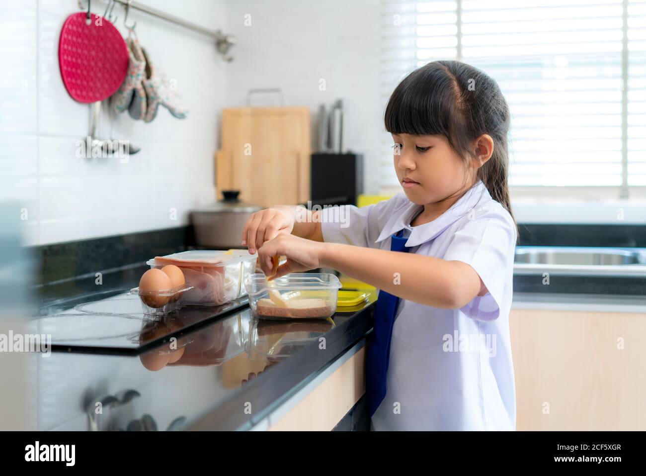 Asiatische Grundschule Schüler Mädchen in Uniform machen Sandwich für Lunch-Box in der morgendlichen Schule Routine für den Tag im Leben immer bereit für die Schule. Stockfoto