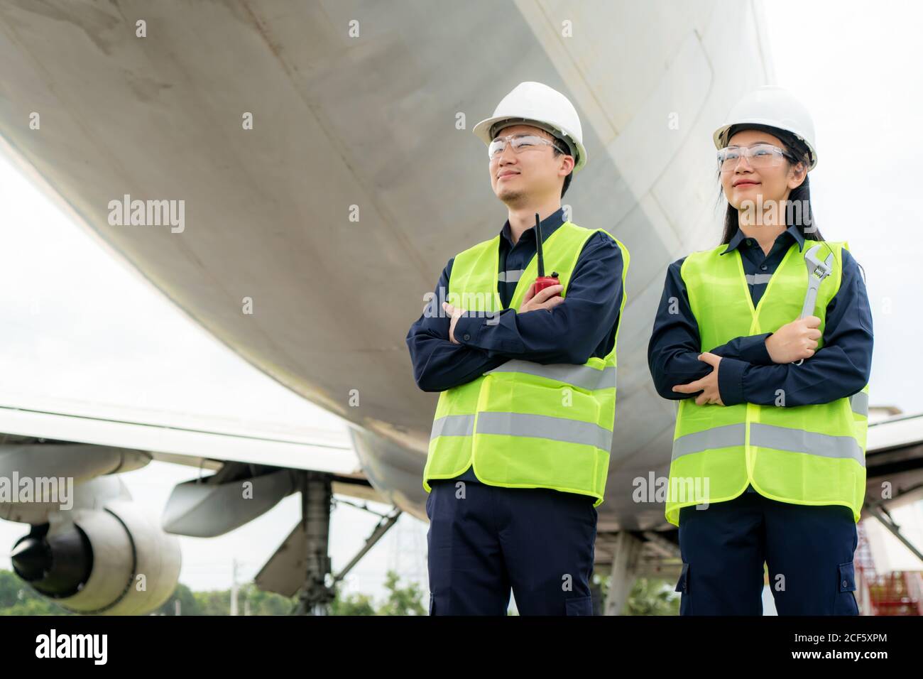 Asian Mann und Frau Ingenieur Wartung Flugzeug Arm gekreuzt und hält Schraubenschlüssel vor Flugzeug von Reparaturen, Fixes, Modernisierung und Renovierung i Stockfoto