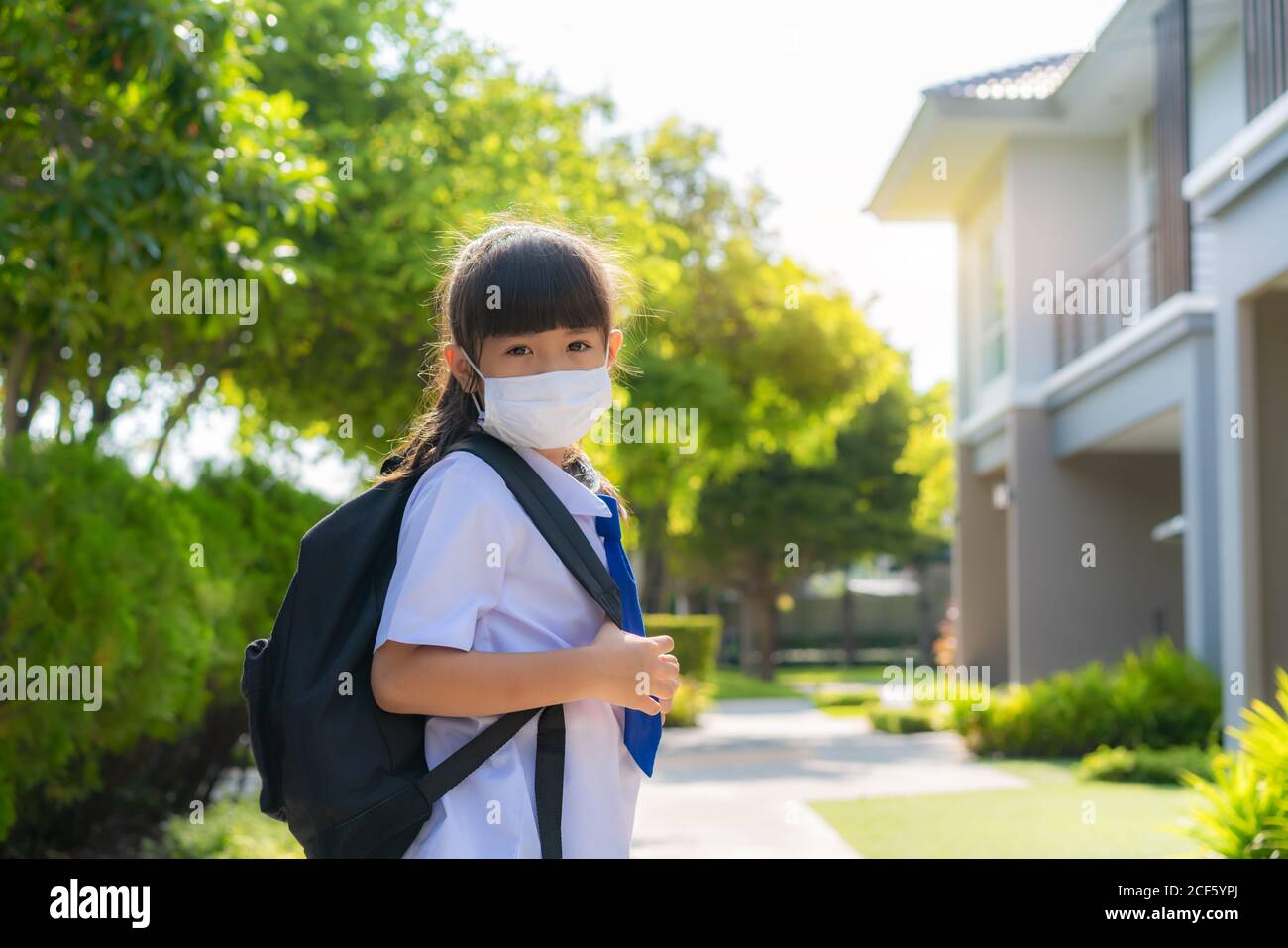 Porträt von niedlichen asiatischen Grundschule Mädchen in medizinische Maske vor zu Hause während COVID-19 Pandemie. Die morgendliche Schulroutine für den Tag im Leben g Stockfoto