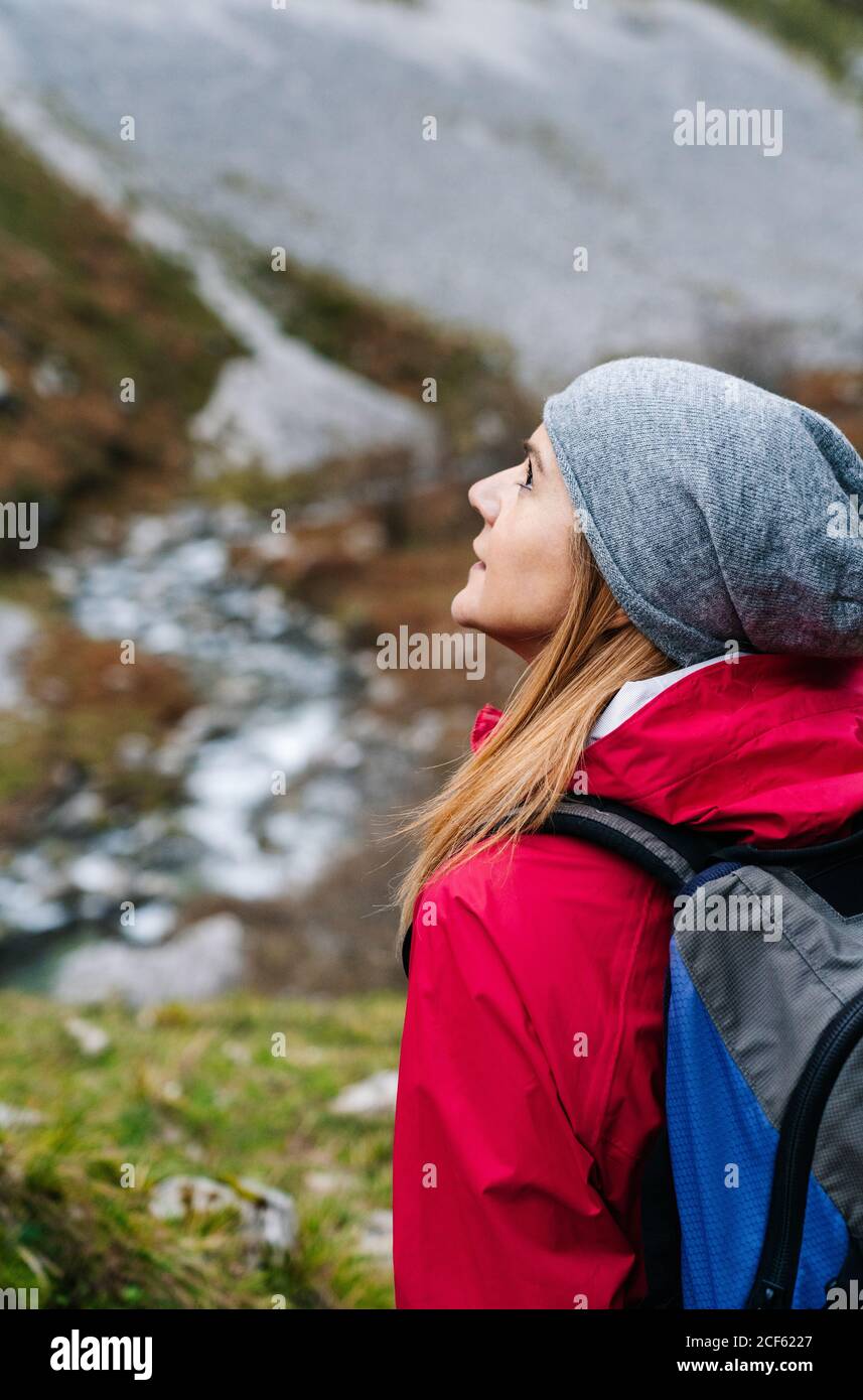 Seitenansicht einer aktiven Wandererin in roter Jacke mit schwerem Rucksack, die beim Wandern in den Bergen Europas, Asturiens, Spaniens, wegschaut Stockfoto