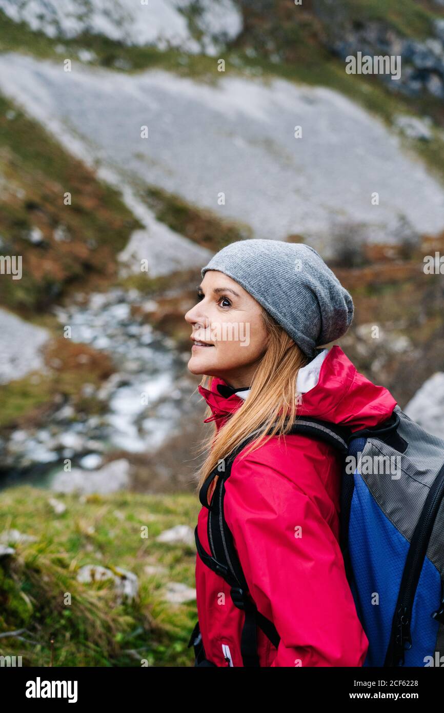 Seitenansicht einer aktiven Wandererin in roter Jacke mit schwerem Rucksack, die beim Wandern in den Bergen Europas, Asturiens, Spaniens, wegschaut Stockfoto