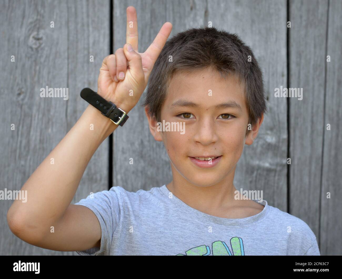 Mixed-race Pre-teen boy (Ostasiatisch und Kaukasisch) zeigt mit seiner rechten Hand das chinesische Handzeichen für die Nummer 2 (Fotoserie: Bild-Nr. 2 von 10). Stockfoto