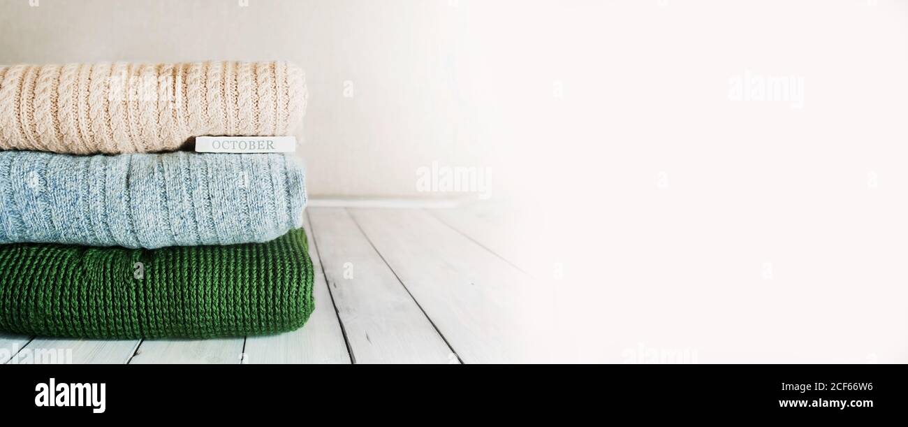 Kuscheliger Herbst-Bannerstapel aus warmen Strickpullover in Pastell Farben und die Inschrift Oktober auf einem hellen Holztisch Im Zimmer Stockfoto