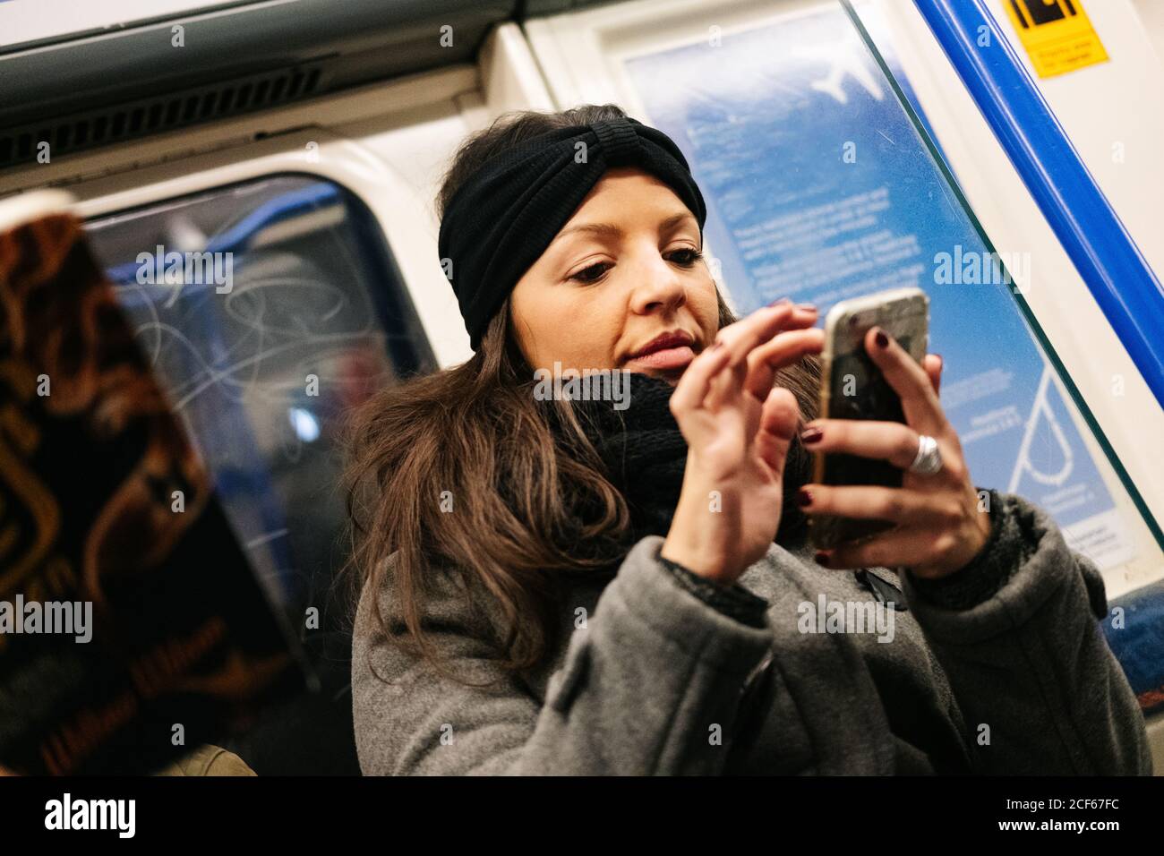 Niedrige Winkel der Dame in lässigem Outfit lächelnd und browsing Smartphone während der Fahrt Zug in U-Bahn in London, Großbritannien Stockfoto