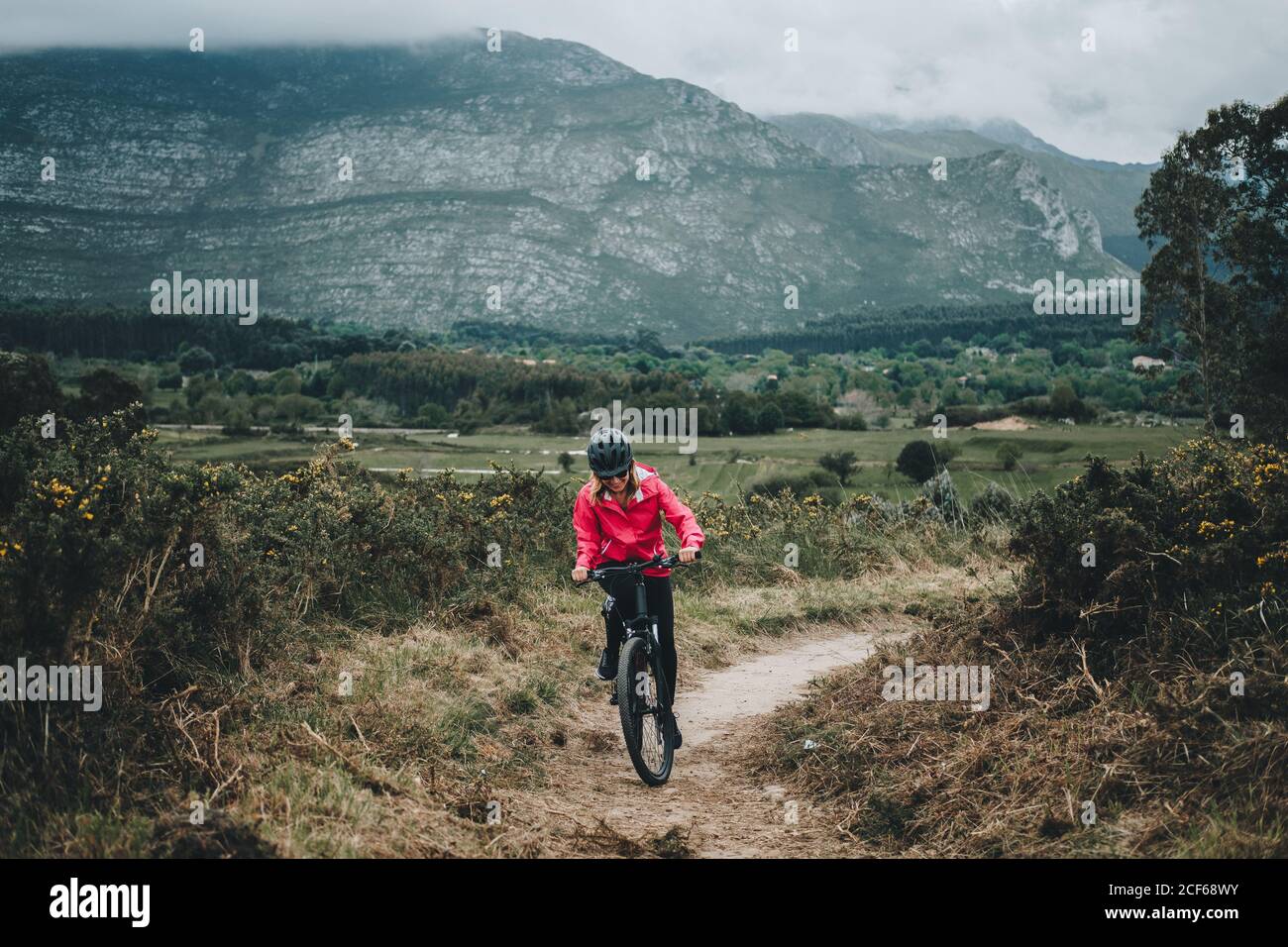 Aktive Frau in Helm und roter Jacke Fahrrad auf Landstraße auf Naturhintergrund reiten Stockfoto