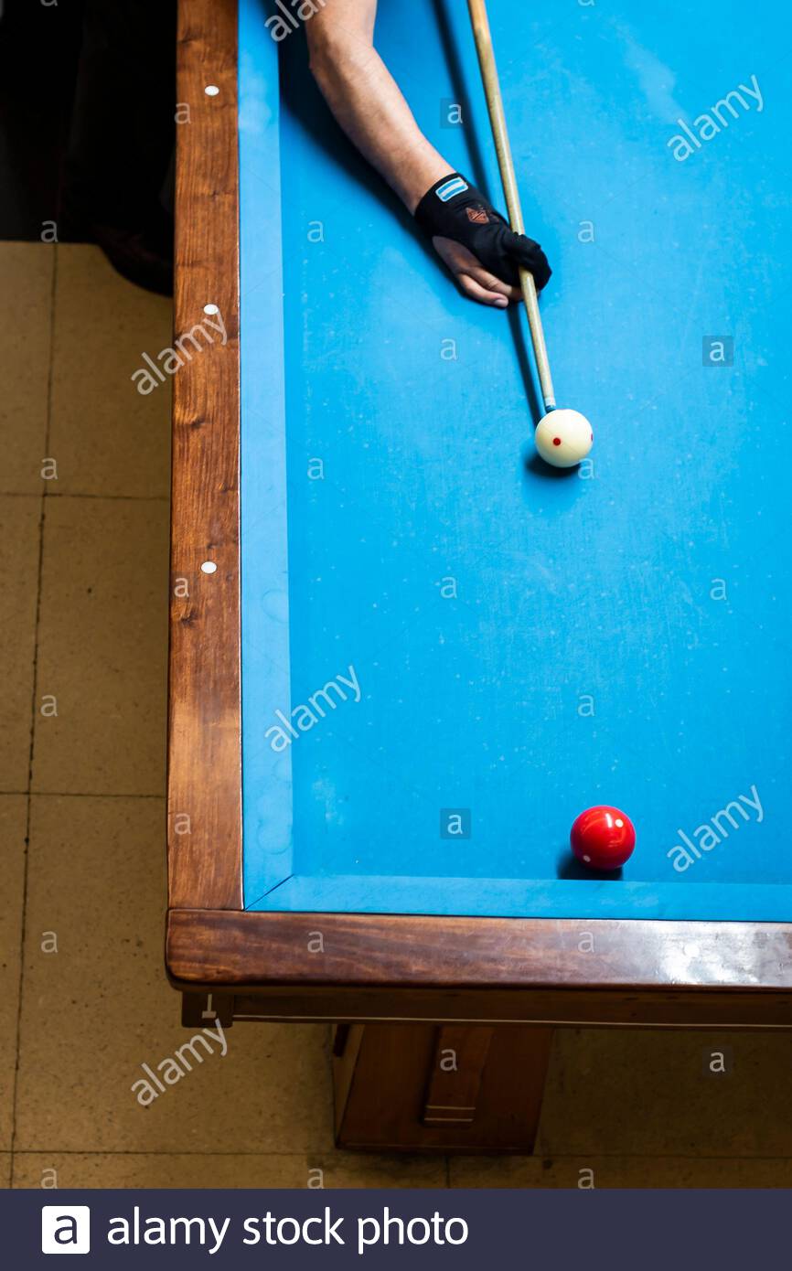 Der Arm des Spielers hält das Queue über dem Billardtisch. Der Spieler hat gerade die weiße Kugel getroffen. Stockfoto