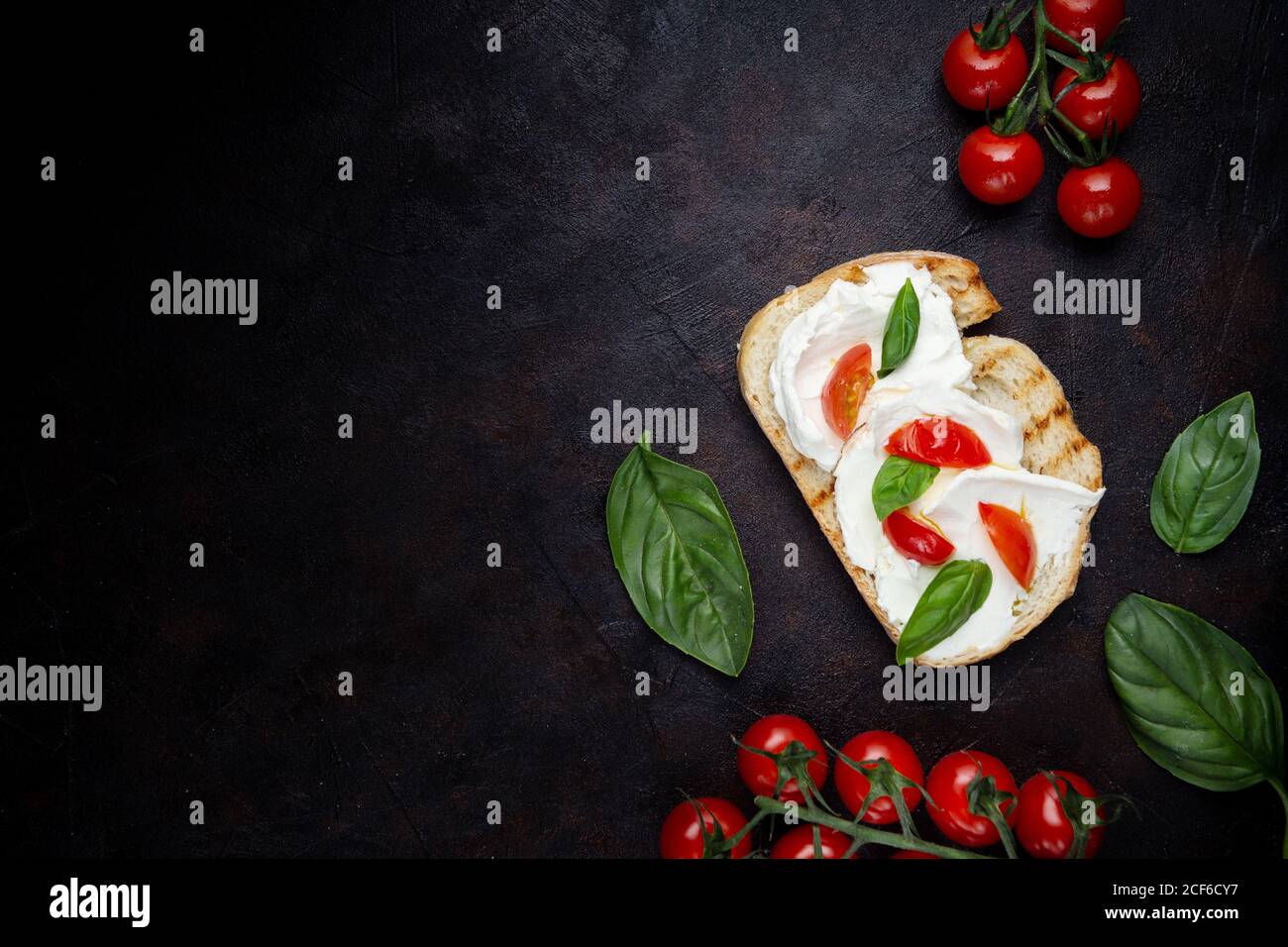 Blick von oben auf knusprigen Toast mit Frischkäse und verschmiert Dekoriert mit Basilikumblättern und Kirschtomaten Schwarzer Hintergrund Stockfoto