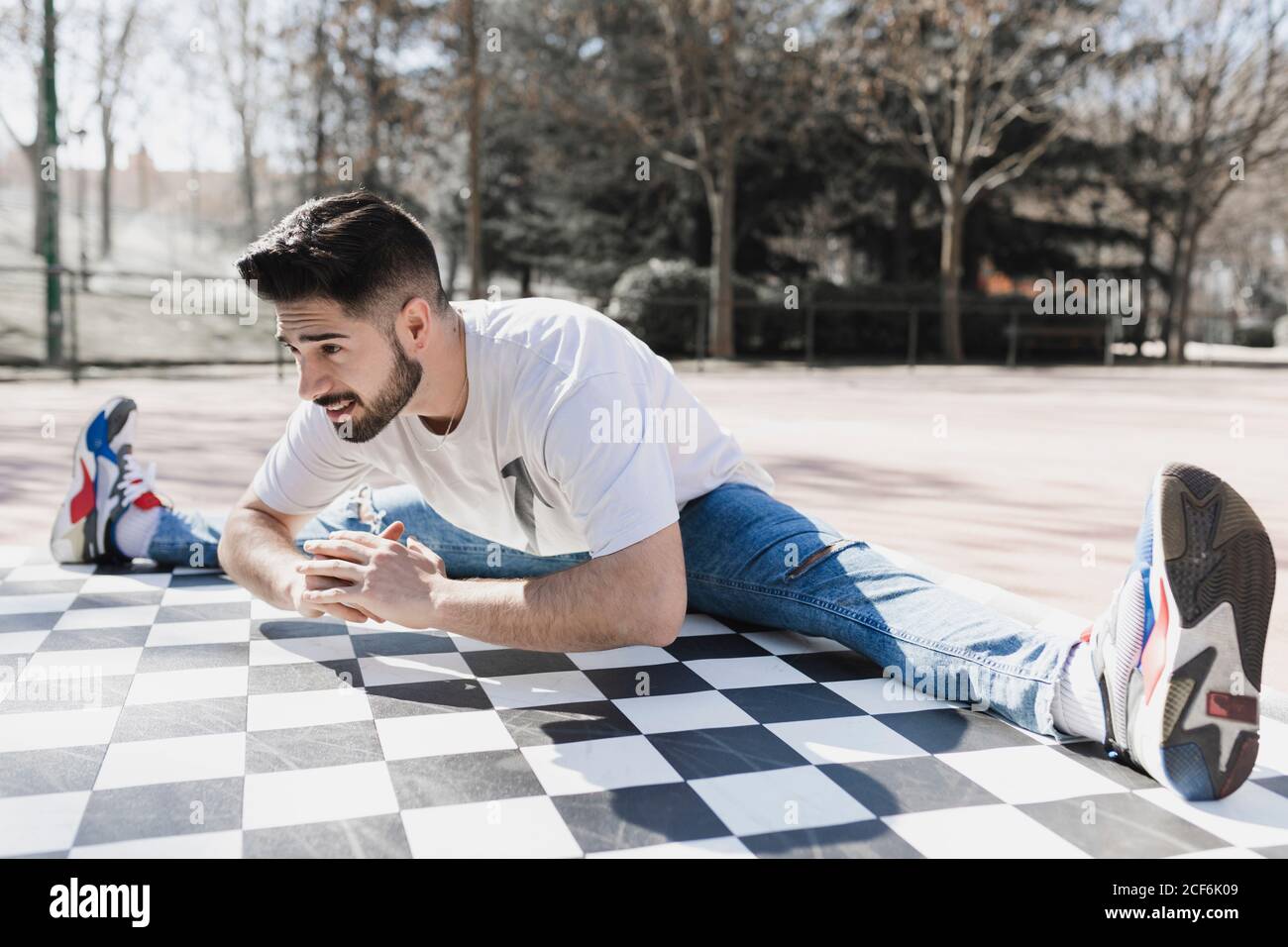 Junge bärtige Kerl in Freizeitkleidung tun Bein Split in parken bei sonnigem Wetter Stockfoto