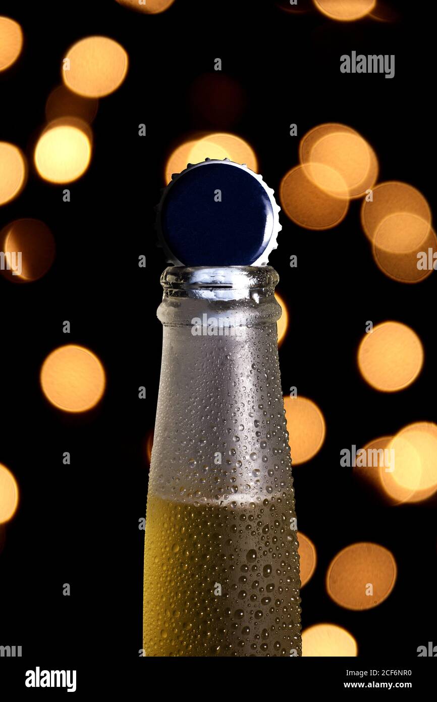 Nahaufnahme des Engpasses von kaltem Bier mit glänzendem Deckel Oben und mit Kondensation auf glasiger Oberfläche gegen verschwommenes Bokeh Leuchtet Stockfoto