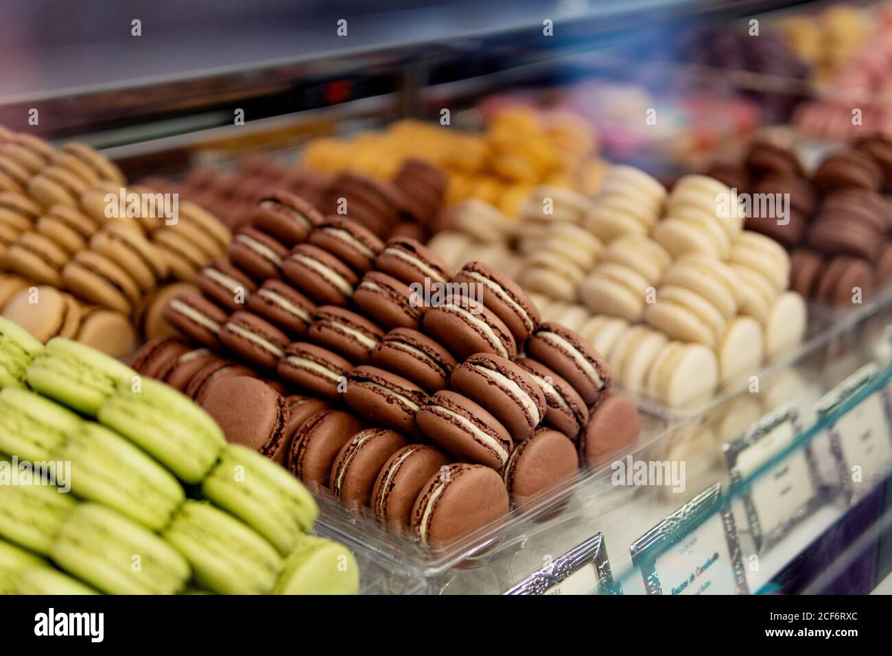 Viele bunte leckere Makronen in verschiedenen Farben mit verschiedenen Füllungen Und schmeckt durch Farben in Behälter, die auf der Schau stehen Fenster in der Konditorei Stockfoto