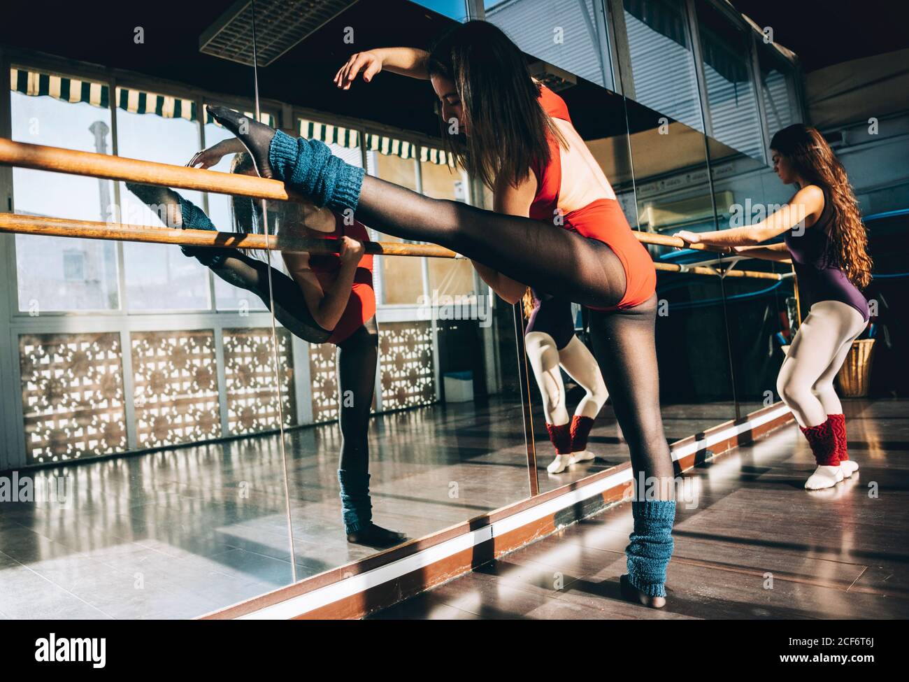 Selbstbewusste junge sportliche Frauen in Bodysuits üben im Ballettstudio Stretching mit Barre. Stockfoto