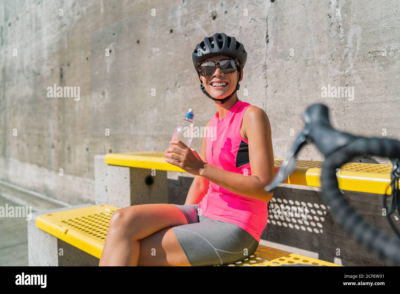 Glücklicher Radfahrer Trinkflasche, müde von Hitze Erschöpfung, eine Pause während der Radtour in der Stadt. Frau, die sich mit dem Rennrad ausruhen und sich mit Wasser versorgen kann Stockfoto