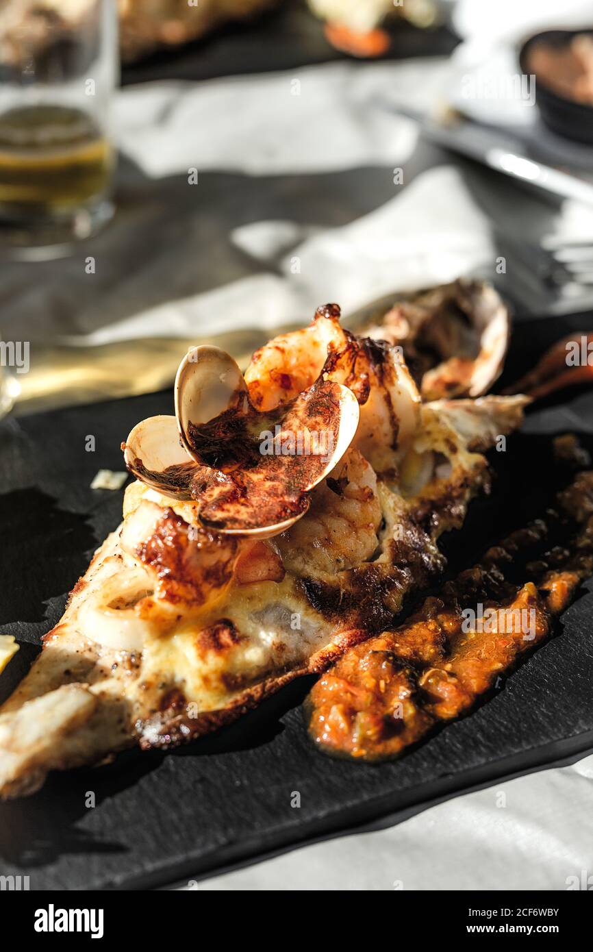 Von oben von leckeren Fisch mit Käse und Schalentieren gebacken Serviert auf Teller mit Sauce auf festlichem Tisch im Restaurant Stockfoto