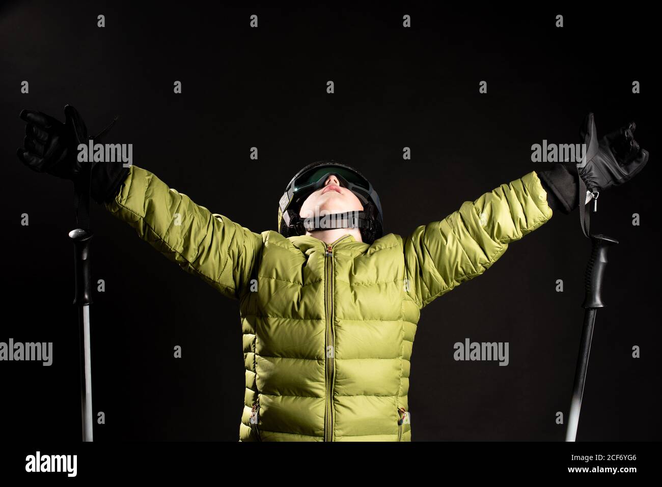 Sportliche kleine Kind trägt Ski-Outfit spreizen Hände mit Ski Sticks auf schwarzem Hintergrund im Studio Stockfoto